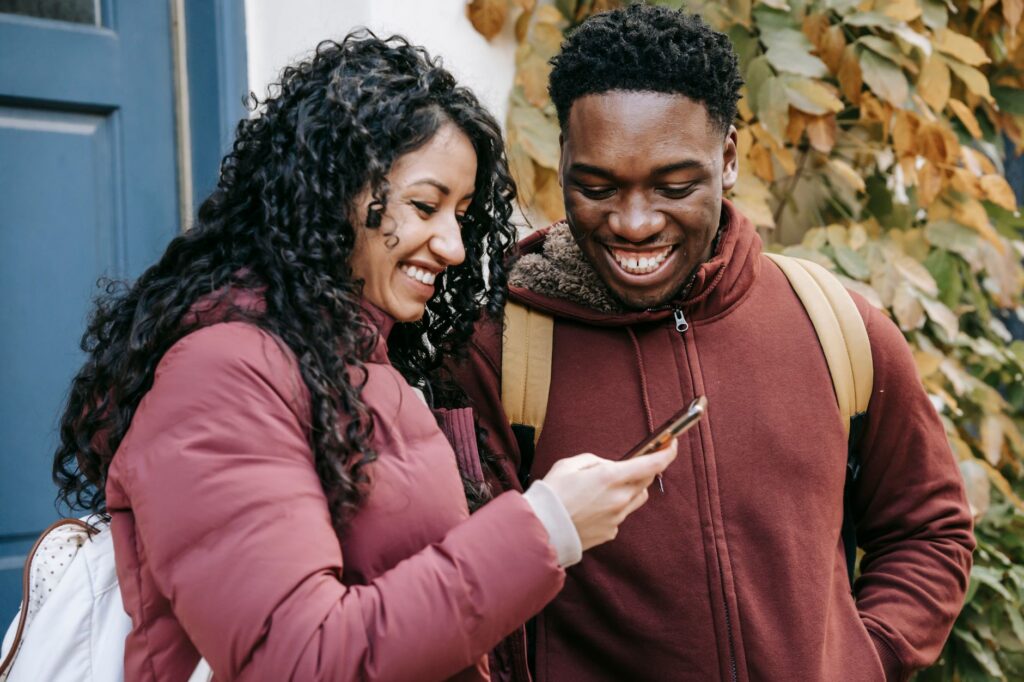 A couple smiling and looking at a phone while walking outdoors