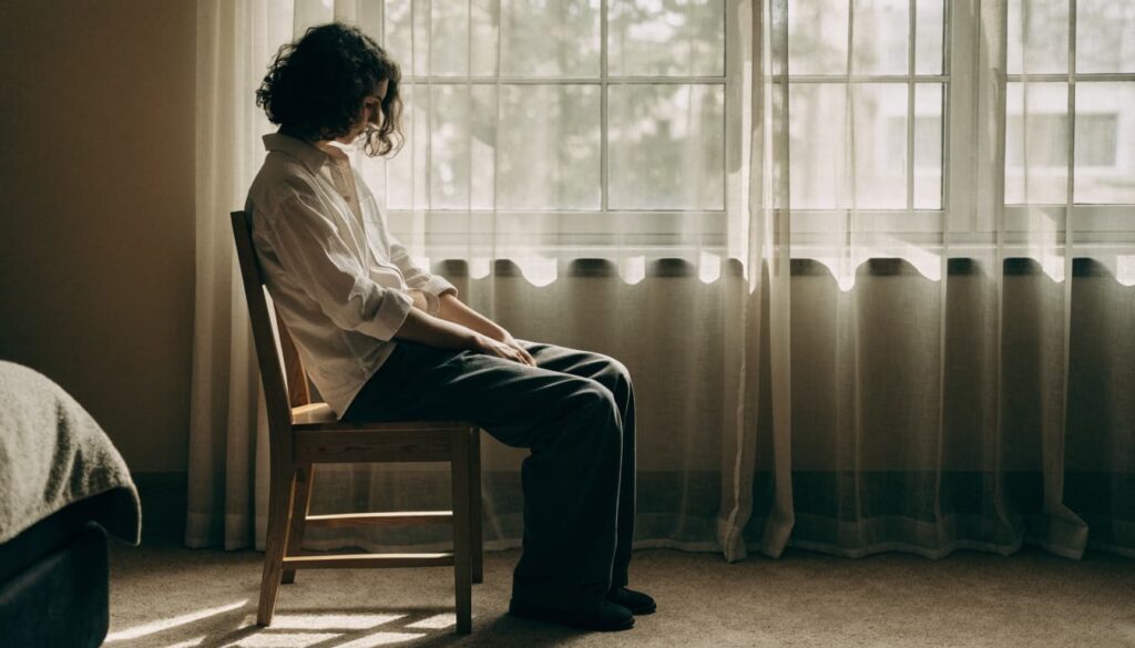 How to Rebuild Trust in a Marriage After It Has Been Broken 3 An adult sits quietly in a chair beside a sunlit window.